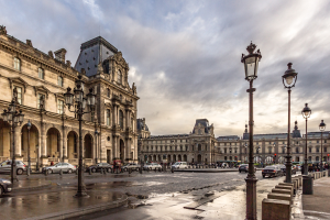 Außenansicht des Louvre-Museums in Paris, Frankreich, mit seiner ikonischen Architektur, Laternenpfählen, Fahrzeugen, Passanten auf dem Gehweg und einer bewölkten Himmel.