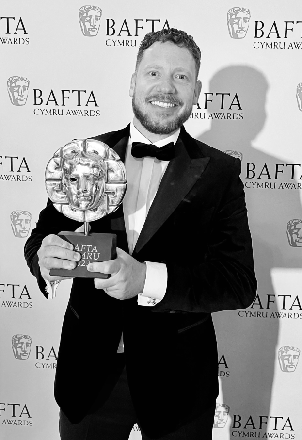 Ein Mann im Smoking hält einen BAFTA-Award und steht vor einem Hintergrund, auf dem "BAFTA Awards 2018" steht.